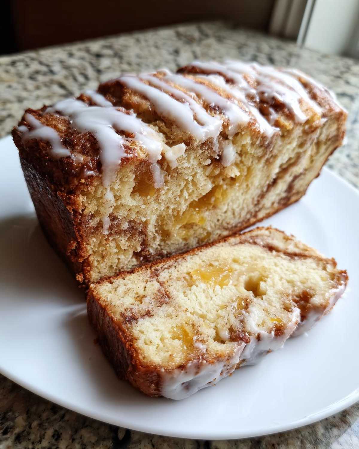 A loaf of apple fritter bread, partially sliced, showing cinnamon swirls and apple chunks, topped with white glaze.