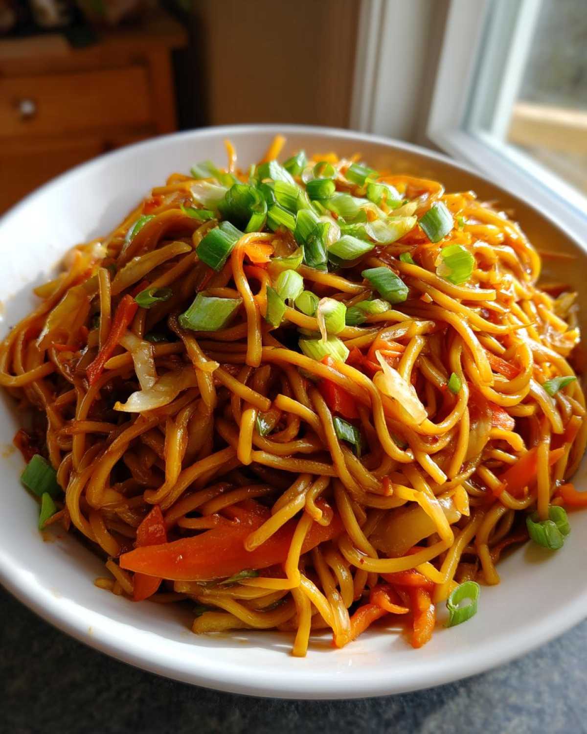 Close-up of a generous serving of saucy fried noodles mixed with carrots and cabbage, topped with fresh green onions.