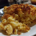 Close-up of a scoop of creamy baked mac and cheese recipe with a golden, crispy breadcrumb topping.