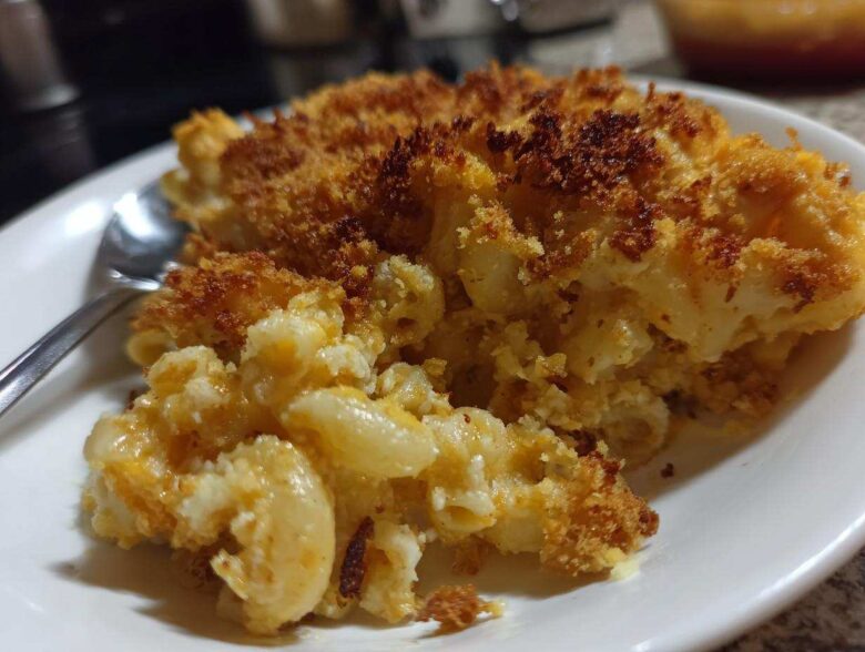 Close-up of a scoop of creamy baked mac and cheese recipe with a golden, crispy breadcrumb topping.