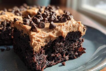 Close-up of a rich, dark chocolate banana bread brownies square topped with peanut butter frosting and mini chocolate chips.
