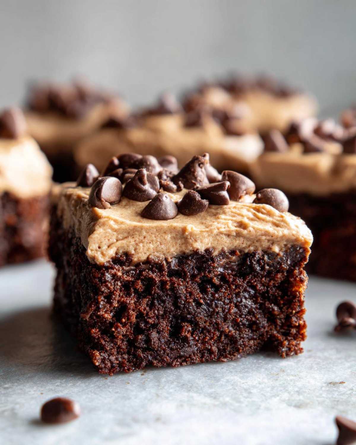 A rich, dark chocolate square of banana bread brownies topped with light brown frosting and mini chocolate chips.