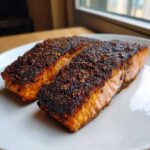 Two perfectly cooked fillets of blackened salmon with a dark, spicy crust resting on a white plate.