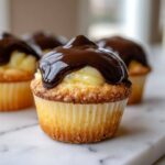 A close-up of a delicious boston cream pie cupcakes filled with vanilla cream and topped with glossy chocolate ganache.