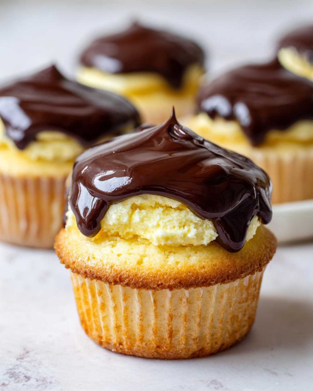 A close-up of one of the delicious boston cream pie cupcakes, featuring vanilla cake, pastry cream, and a thick chocolate ganache topping.