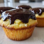 Close-up of a Boston cream pie cupcake filled with custard and topped with dripping dark chocolate ganache.