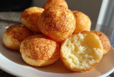 A stack of freshly baked brazilian cheese bread rolls with a golden crust, one is broken open showing the airy interior.
