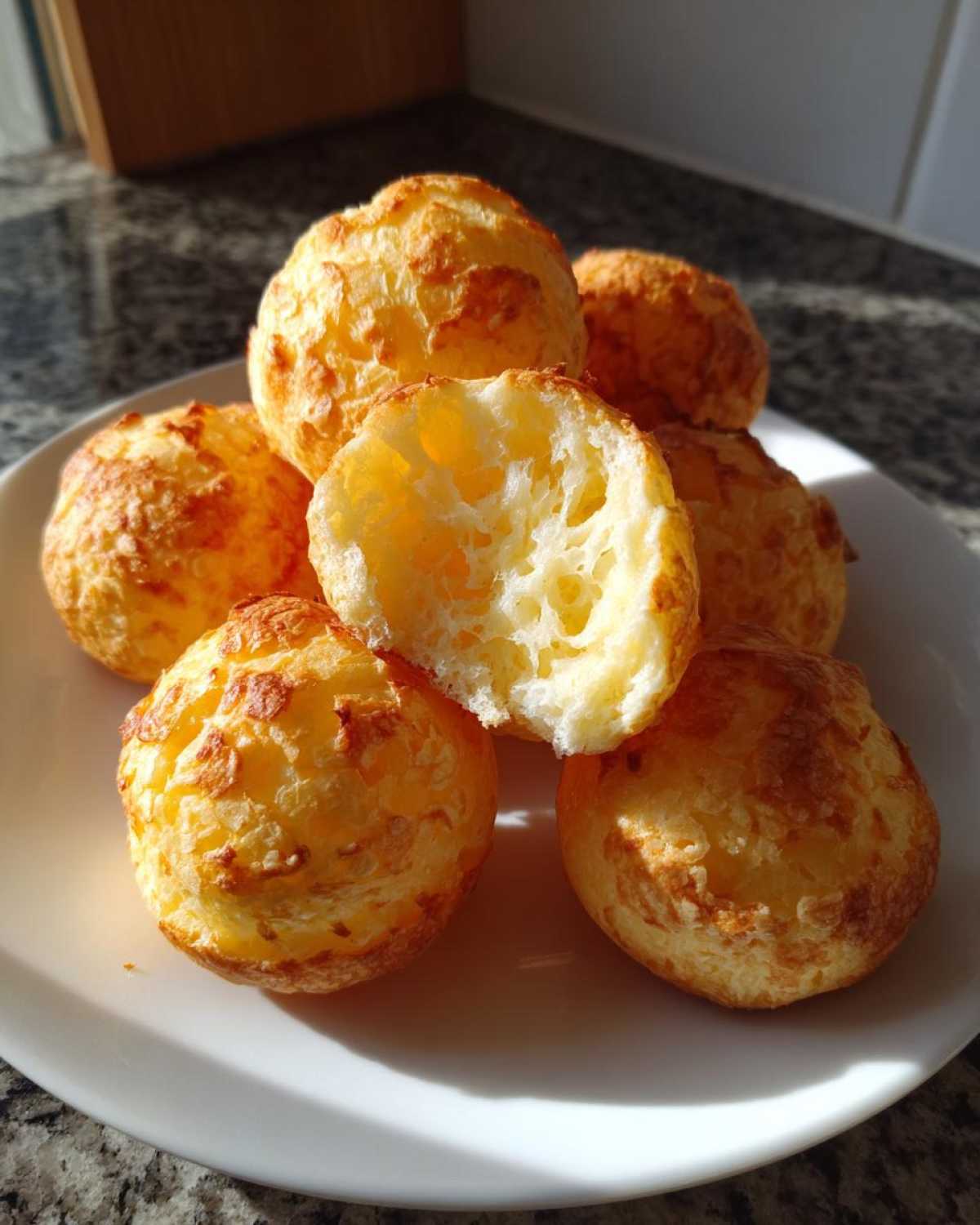 A stack of golden, baked brazilian cheese bread puffs, one broken open showing the airy interior.