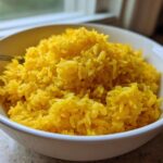 A close-up of fluffy, bright yellow turmeric rice served in a white bowl.