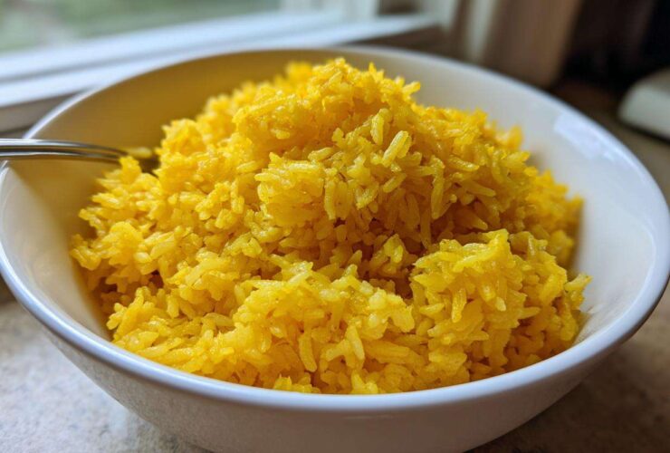 A close-up of fluffy, bright yellow turmeric rice served in a white bowl.