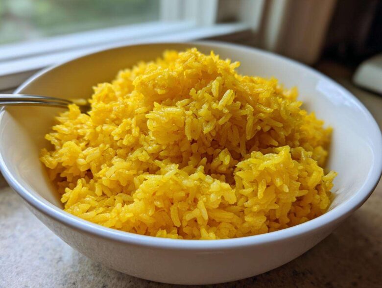 A close-up of fluffy, bright yellow turmeric rice served in a white bowl.