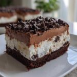 A close-up of a layered brownie refrigerator cake slice topped with chocolate mousse and mini chocolate chips.