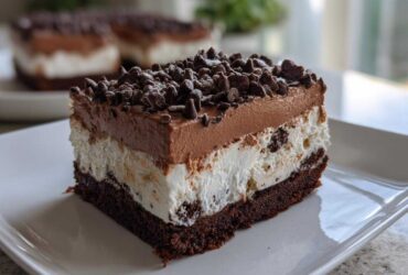 A close-up of a layered brownie refrigerator cake slice topped with chocolate mousse and mini chocolate chips.
