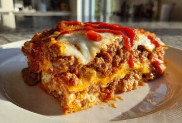 Close-up of a hearty slice of burrito bake layered with meat, cheese, and topped with sauce.