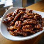 A close-up of shiny, brown candied pecans piled high in a small white bowl.
