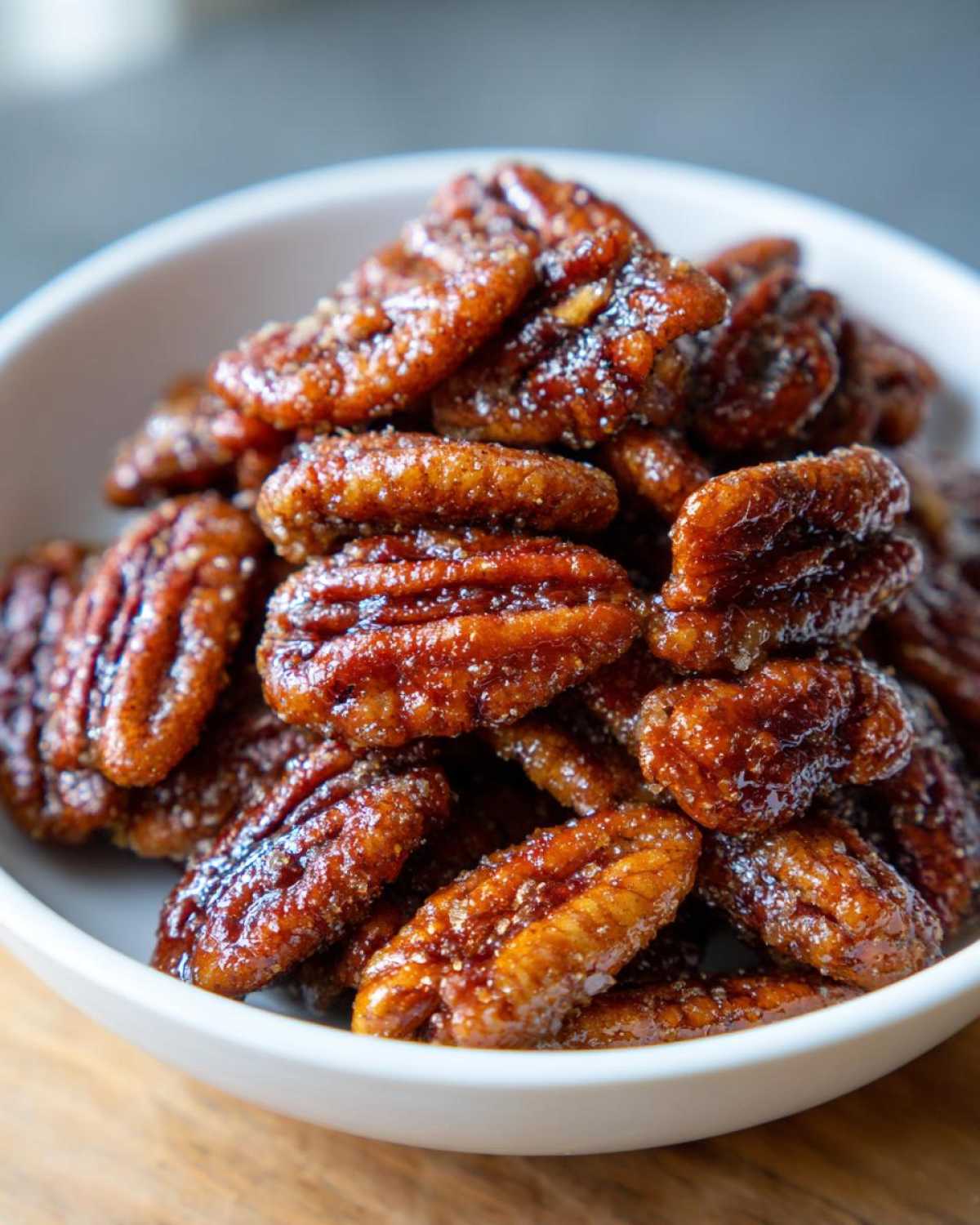 Close-up shot of shiny, caramelized candied pecans piled high in a small white bowl.