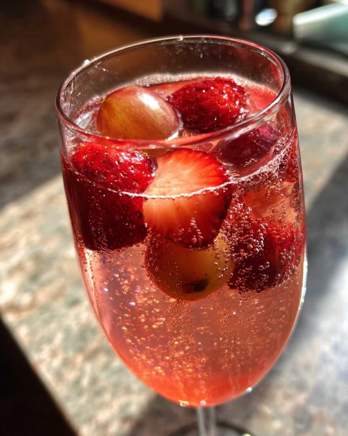 Close-up of a flute glass filled with bubbly, pink champagne punch garnished with strawberries and grapes.