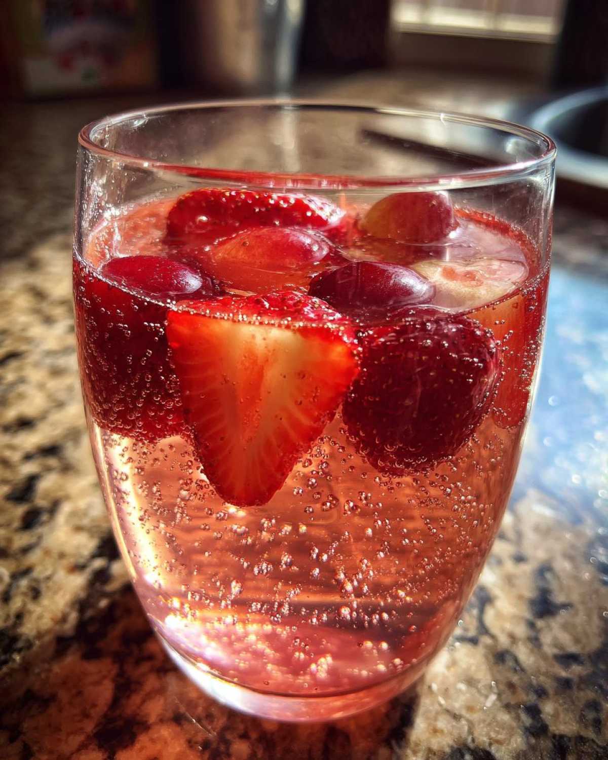 Close-up of a glass filled with bubbly pink champagne punch, garnished with fresh strawberry slices and grapes.