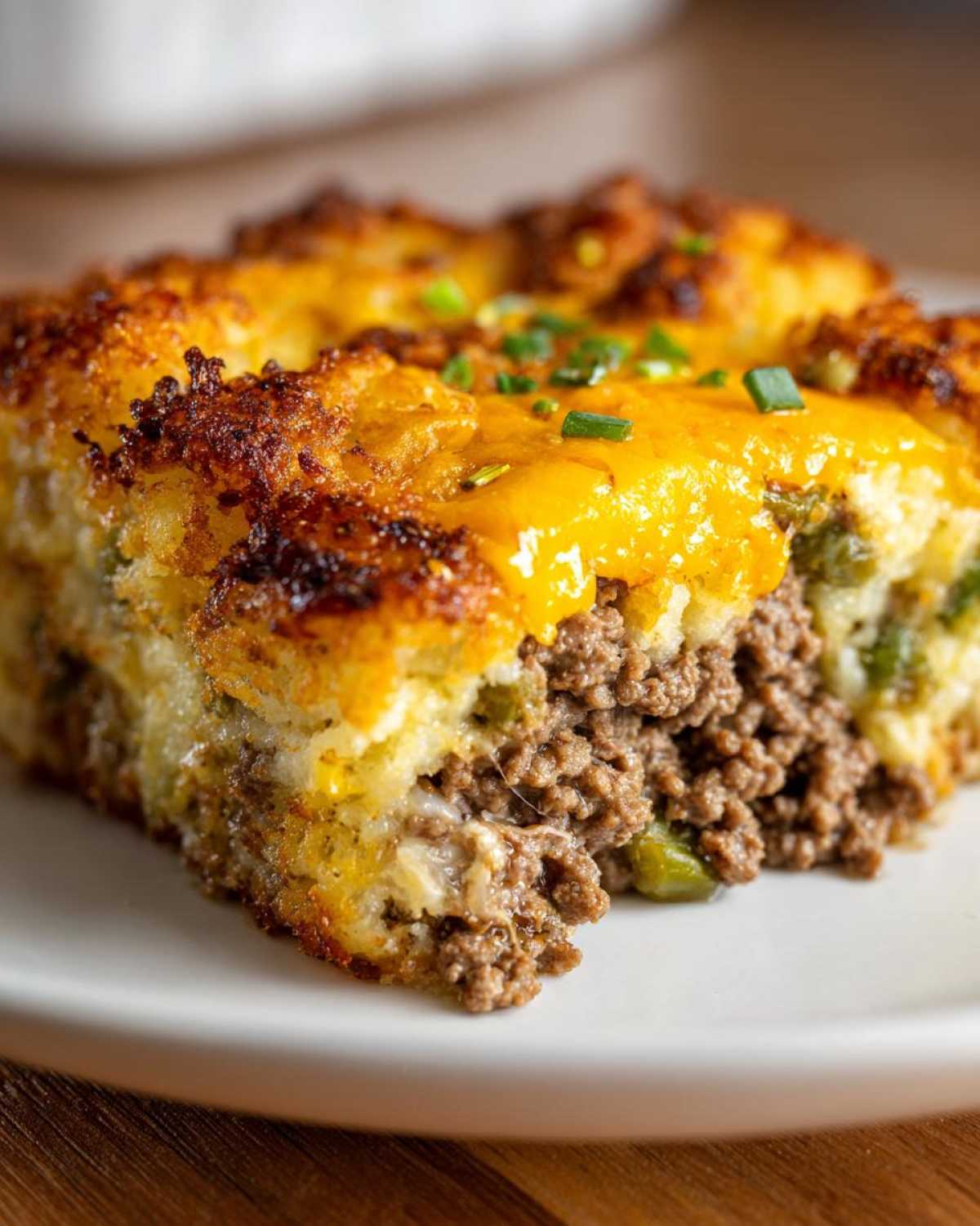 A close-up view of a serving of tater tot casserole showing crispy potato topping, melted cheddar cheese, and seasoned ground beef filling.