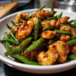 Close-up of glossy, saucy chicken and green beans tossed together in a white bowl.