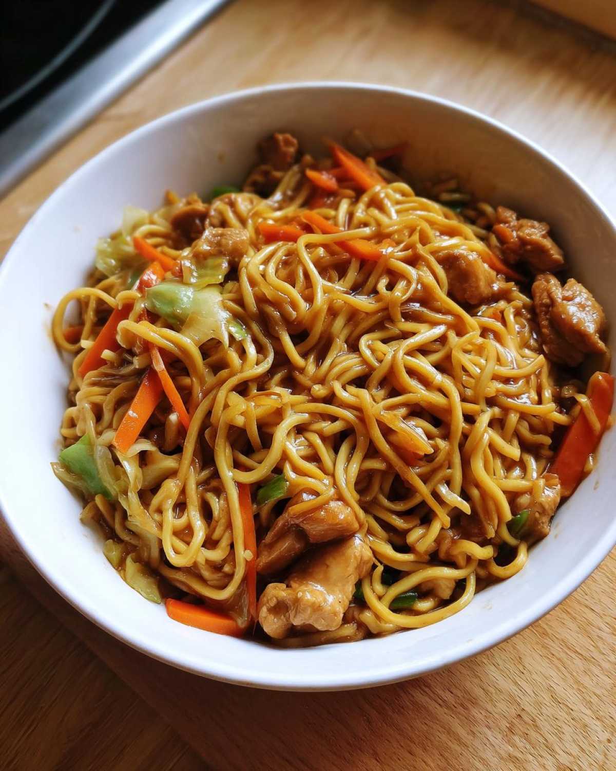 A white bowl filled with glossy noodles, chicken pieces, and sliced carrots from the chicken chow mein recipe.