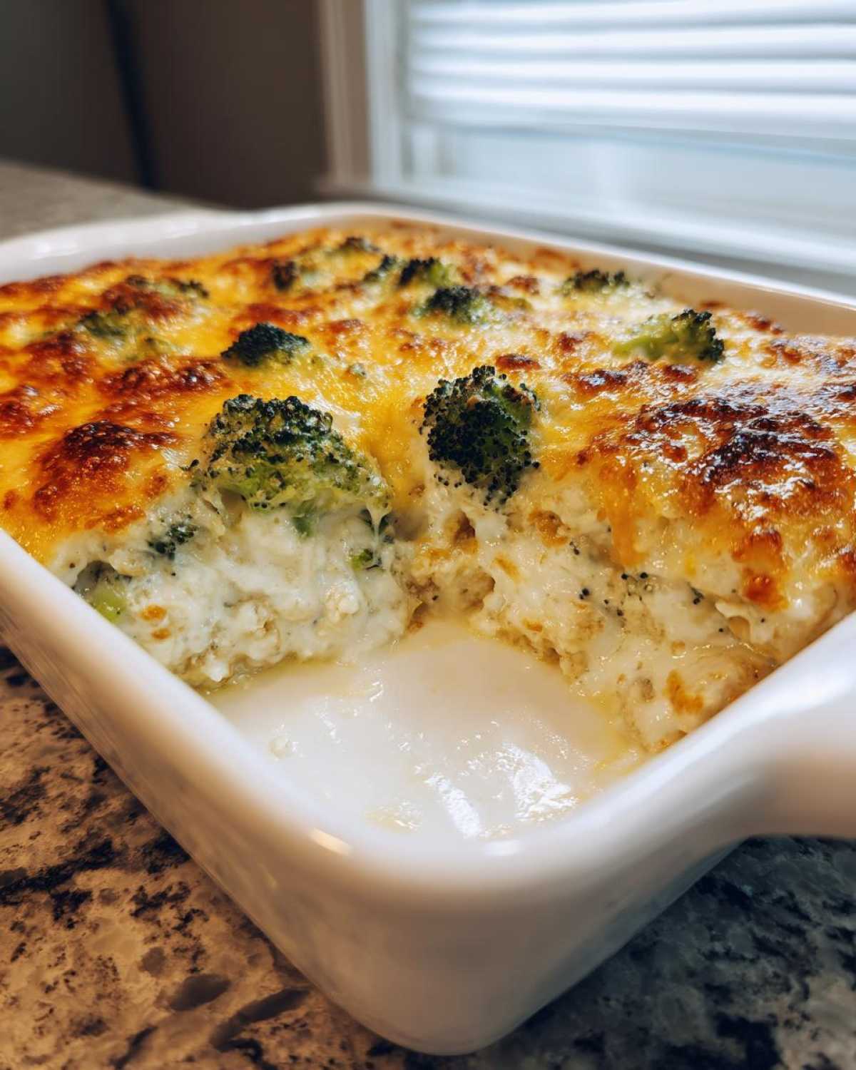 A serving dish of creamy Chicken Divan casserole topped with melted, browned cheese and broccoli florets.