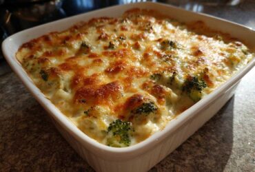 A close-up of a bubbling, cheesy Chicken Divan casserole baked in a white square dish.