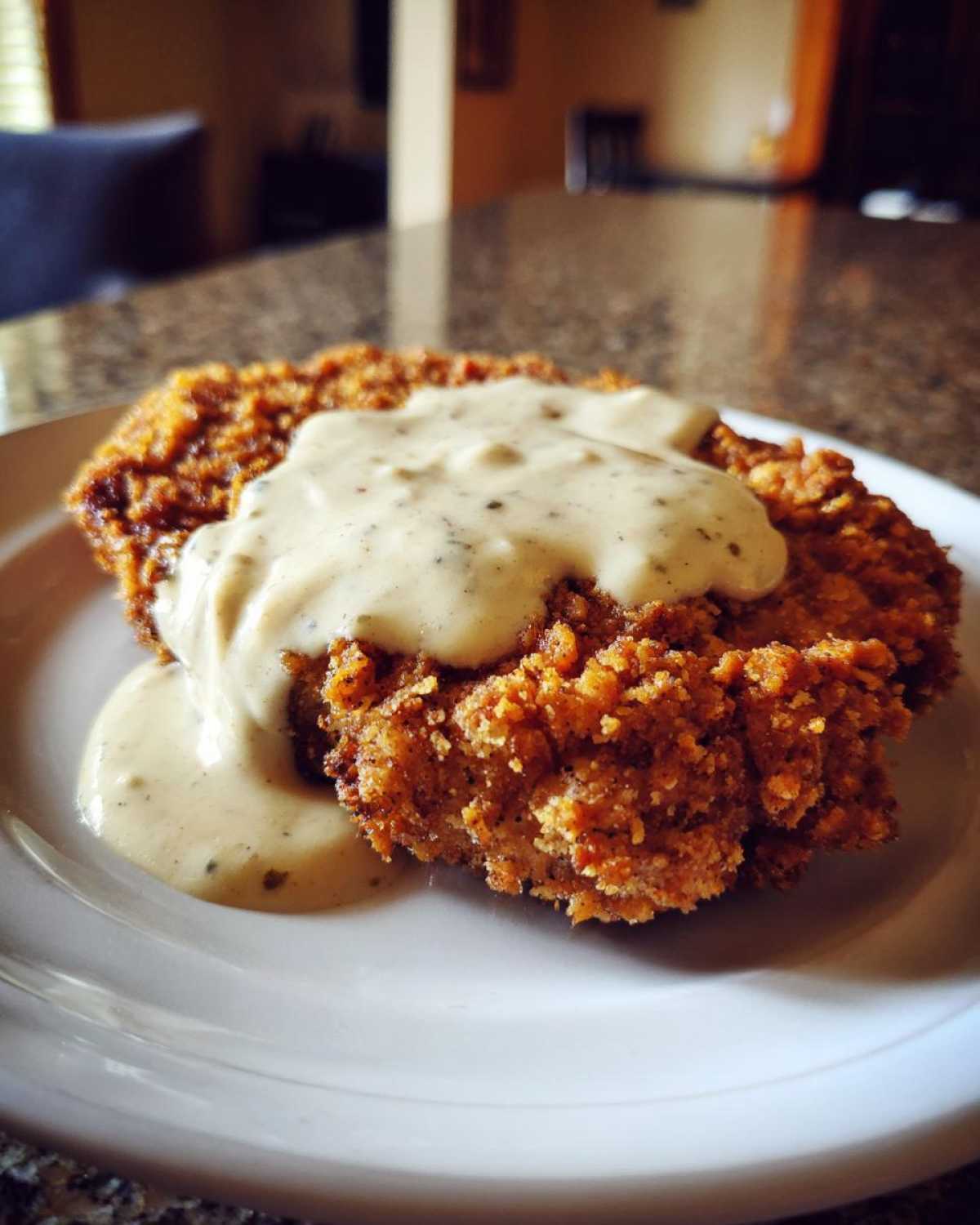 Close-up of a crispy, golden brown chicken fried steak smothered in creamy, peppered country gravy.