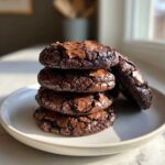A stack of four rich, fudgy chocolate brownie cookies with cracked tops, resting on a white plate.
