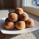 A mound of freshly made cinnamon sugar snowball cookies coated heavily in sparkling cinnamon sugar mix.