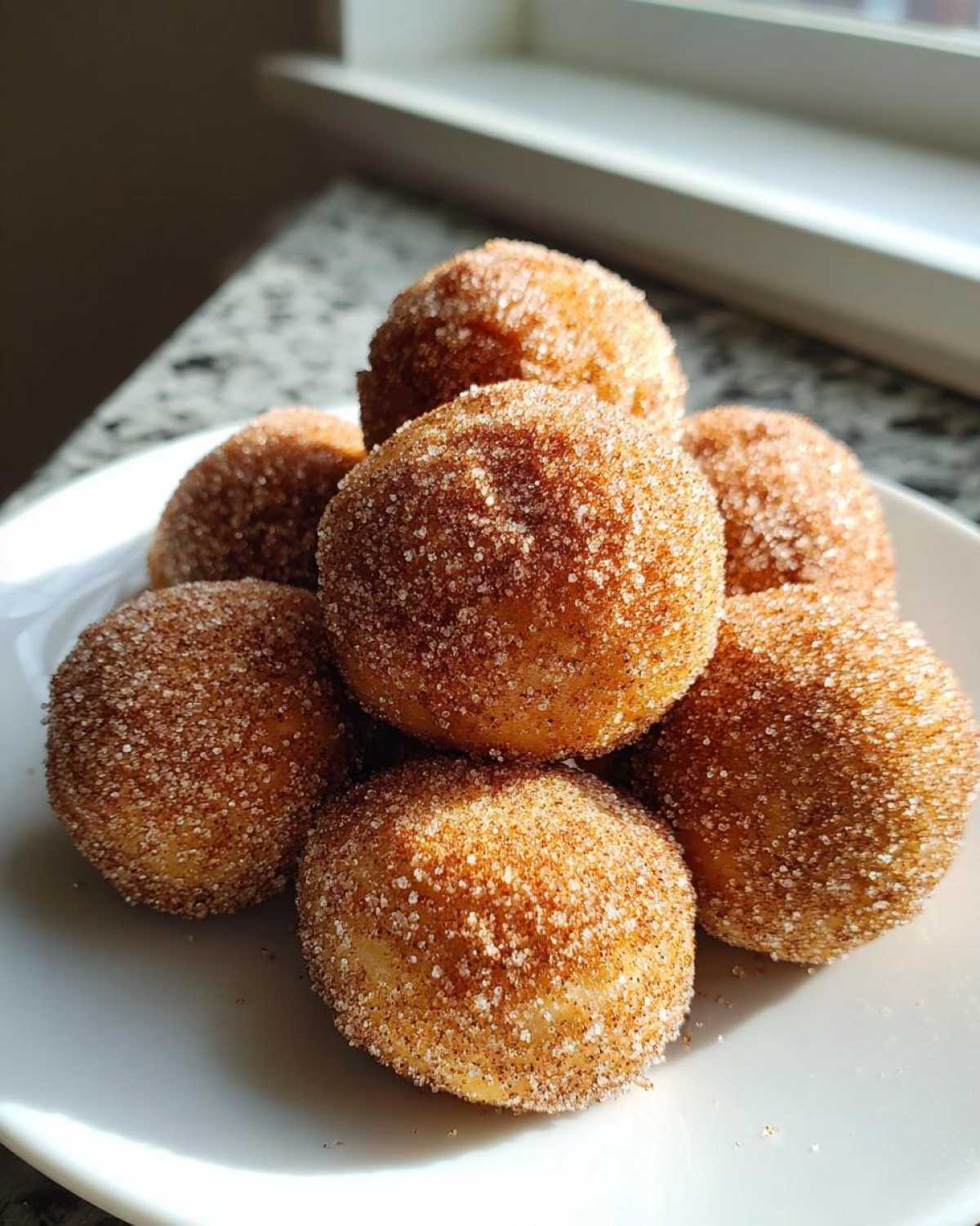 A close-up of several freshly made cinnamon sugar snowball cookies piled high on a white plate, glistening with sugar.