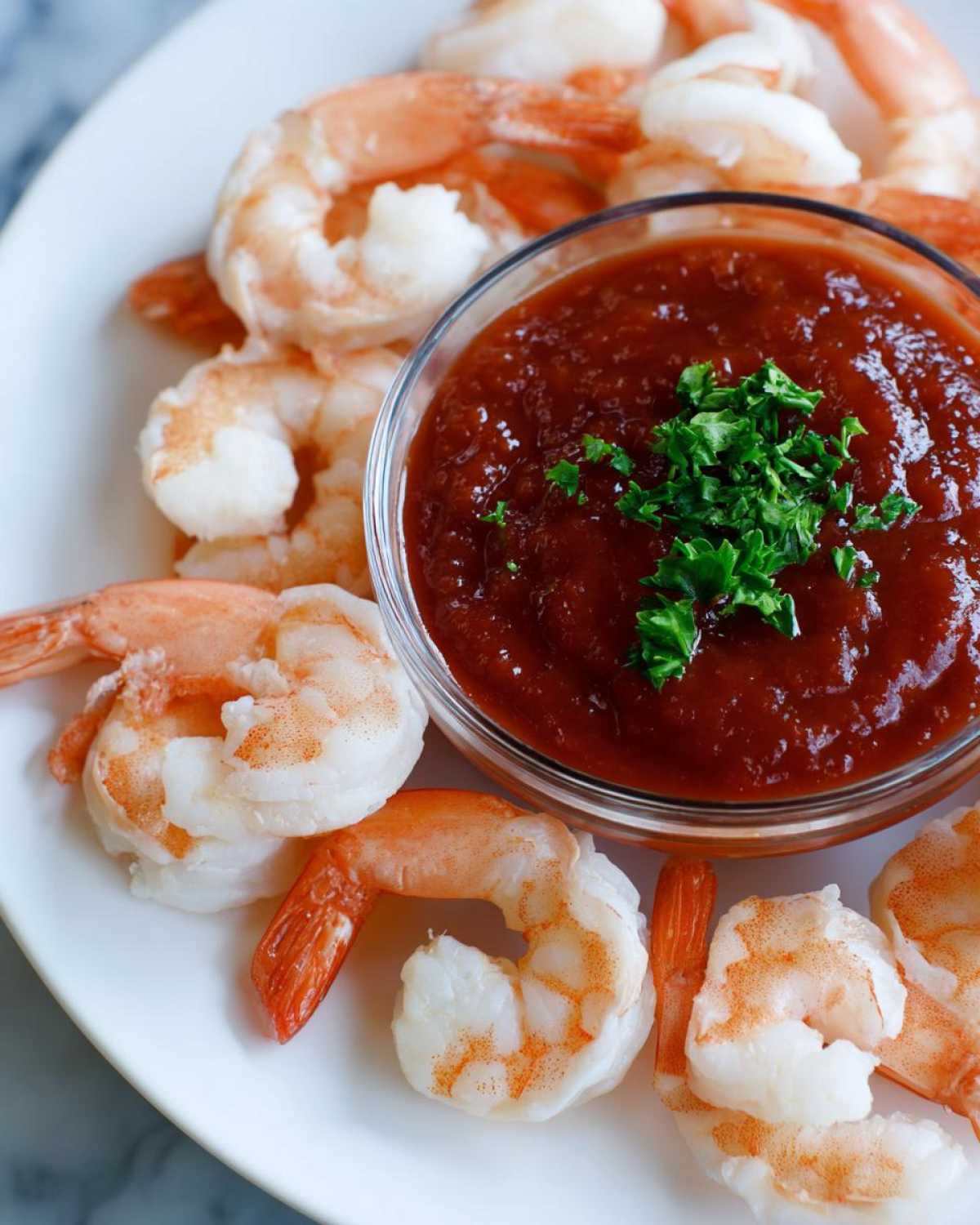 Close-up of cooked, peeled shrimp arranged around a glass bowl of red cocktail sauce for a perfect shrimp cocktail.