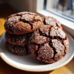 A stack of dark, cracked ginger molasses cookies heavily coated in sparkling white sugar, displayed on a light plate.