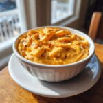 Close-up of creamy, orange beer cheese dip topped with black pepper in a white bowl.