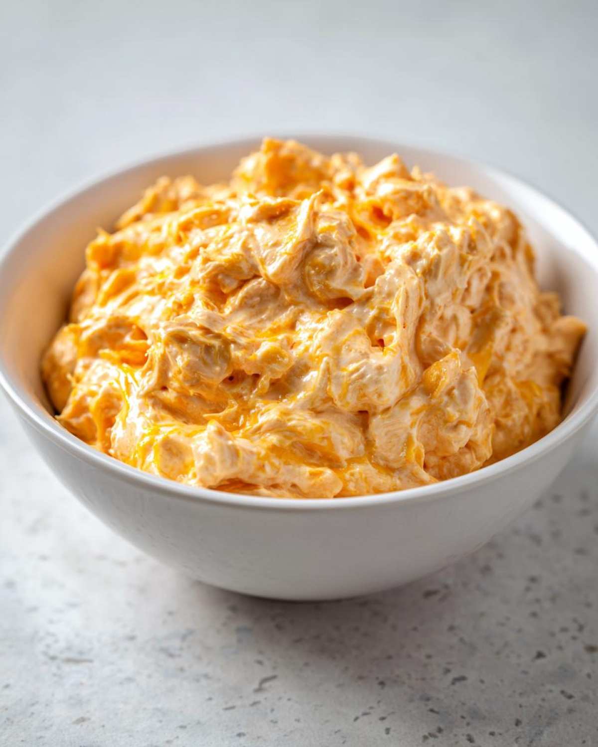 Close-up of rich, creamy beer cheese dip with an orange hue served in a white bowl.