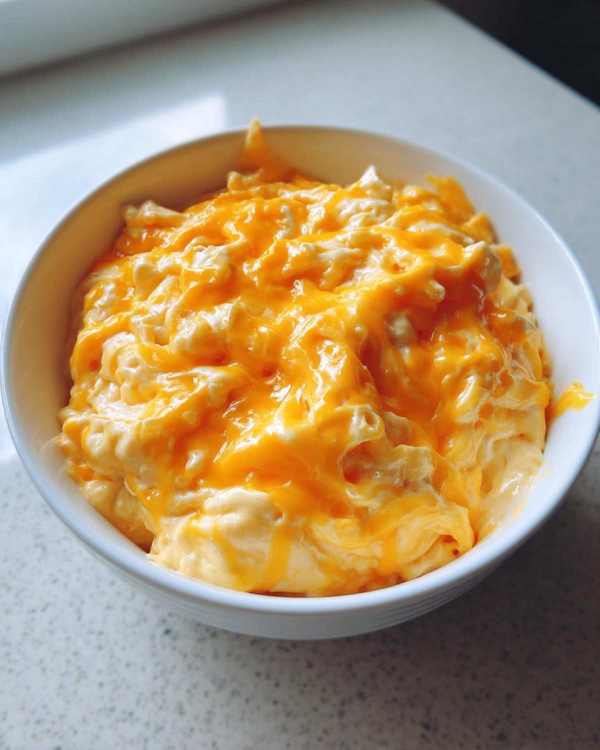 Close-up of creamy beer cheese dip topped with melted sharp cheddar cheese in a white bowl.