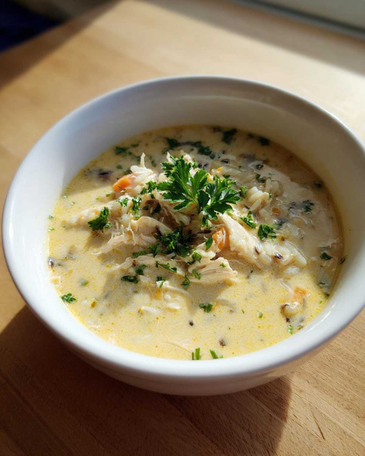 A close-up of a creamy chicken wild rice soup, garnished with fresh parsley, served in a white bowl.