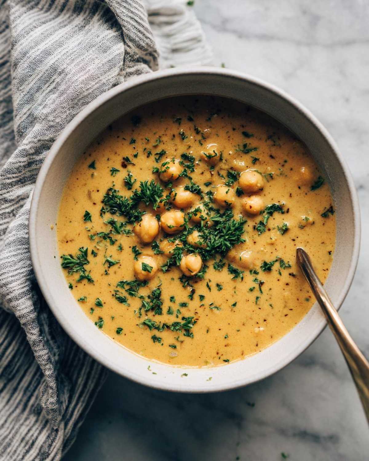 Overhead view of a creamy, golden chickpea soup garnished with whole chickpeas and fresh chopped parsley.