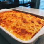 Close-up of a baked, creamy corn dip topped with bubbling, golden-brown melted cheddar cheese.