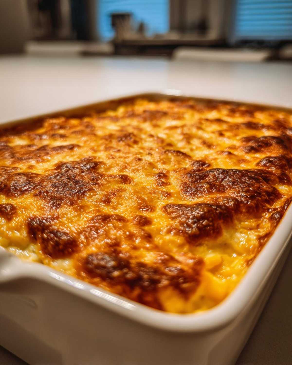 Close-up of a creamy corn dip baked in a white dish with a beautifully browned and bubbly cheese topping.