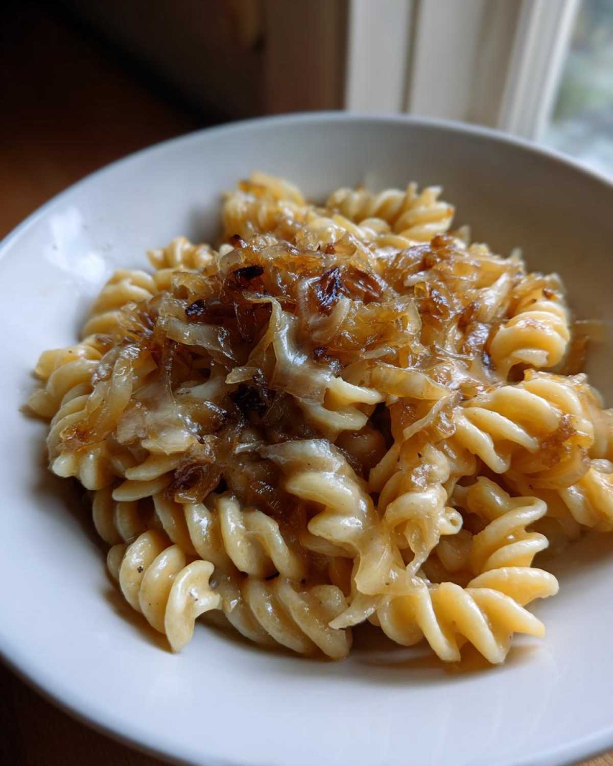 A close-up of a white bowl filled with creamy french onion pasta topped generously with caramelized onions.