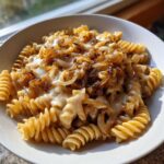 A white bowl filled with creamy french onion pasta topped generously with deeply caramelized onions.