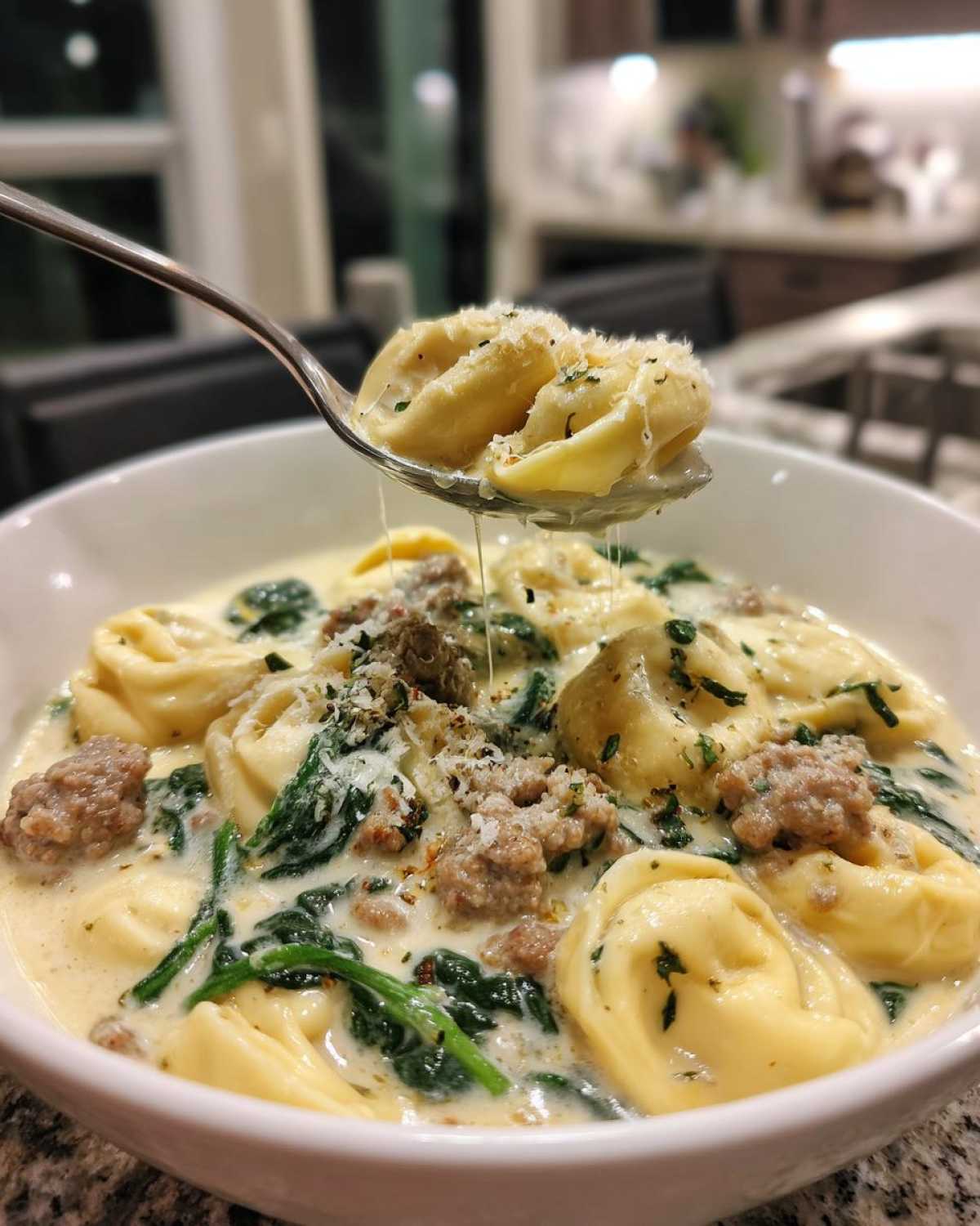 A spoonful of tortellini is lifted from a bowl of creamy sausage tortellini soup topped with parmesan.