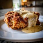 A close-up of a perfectly breaded and fried chicken fried steak smothered in creamy, black pepper gravy.