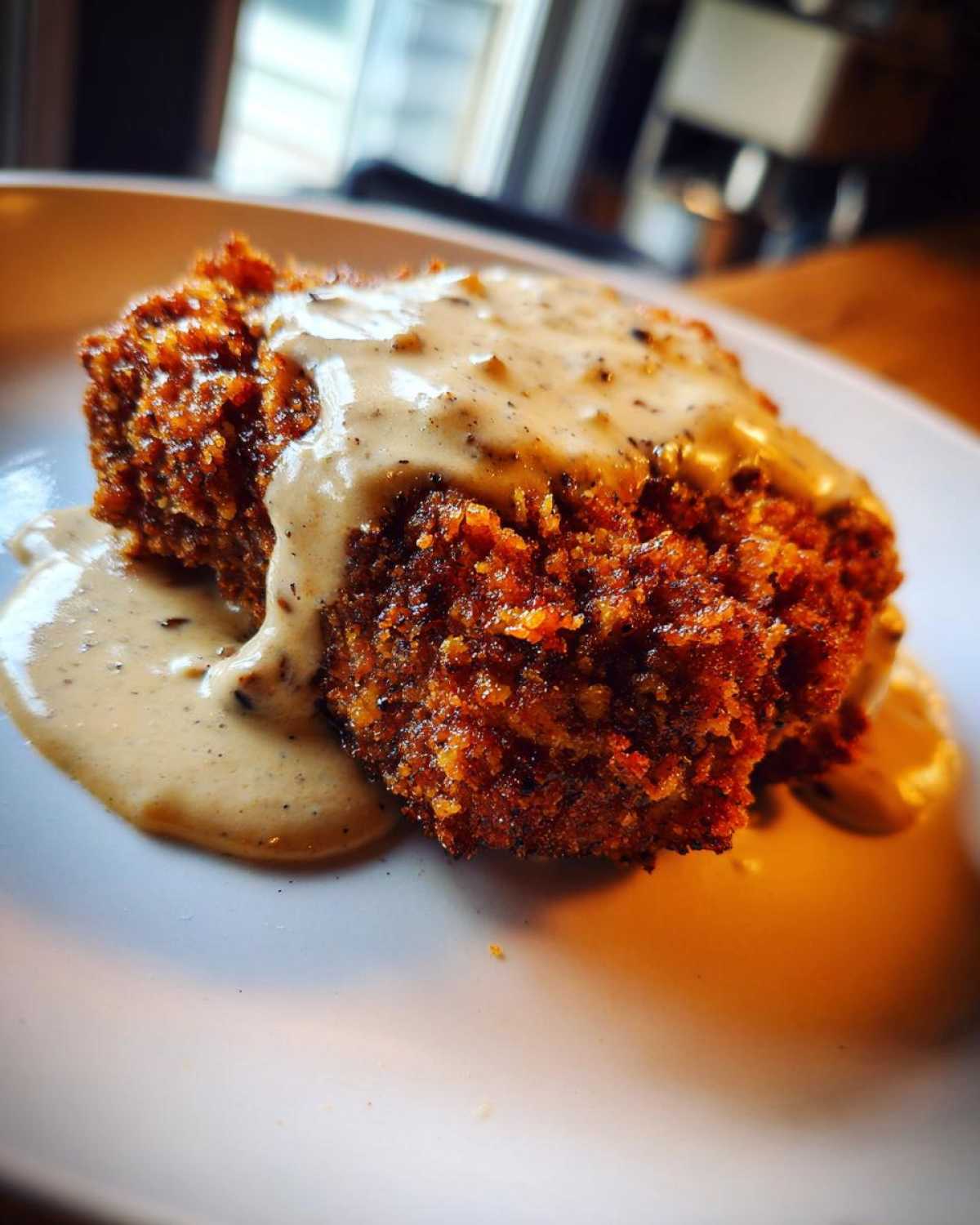 Close-up of a golden brown, crispy chicken fried steak smothered in creamy, peppered gravy.