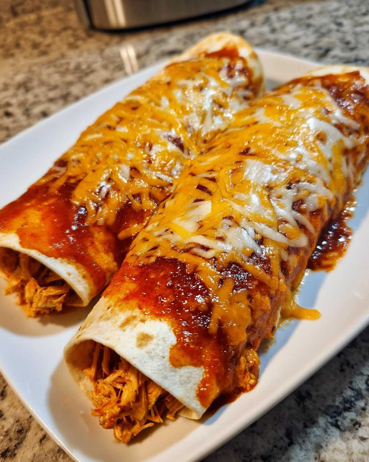 Two rolled tortillas filled with shredded chicken, smothered in red sauce and topped with melted cheddar and Monterey Jack cheese, representing easy chicken enchiladas.