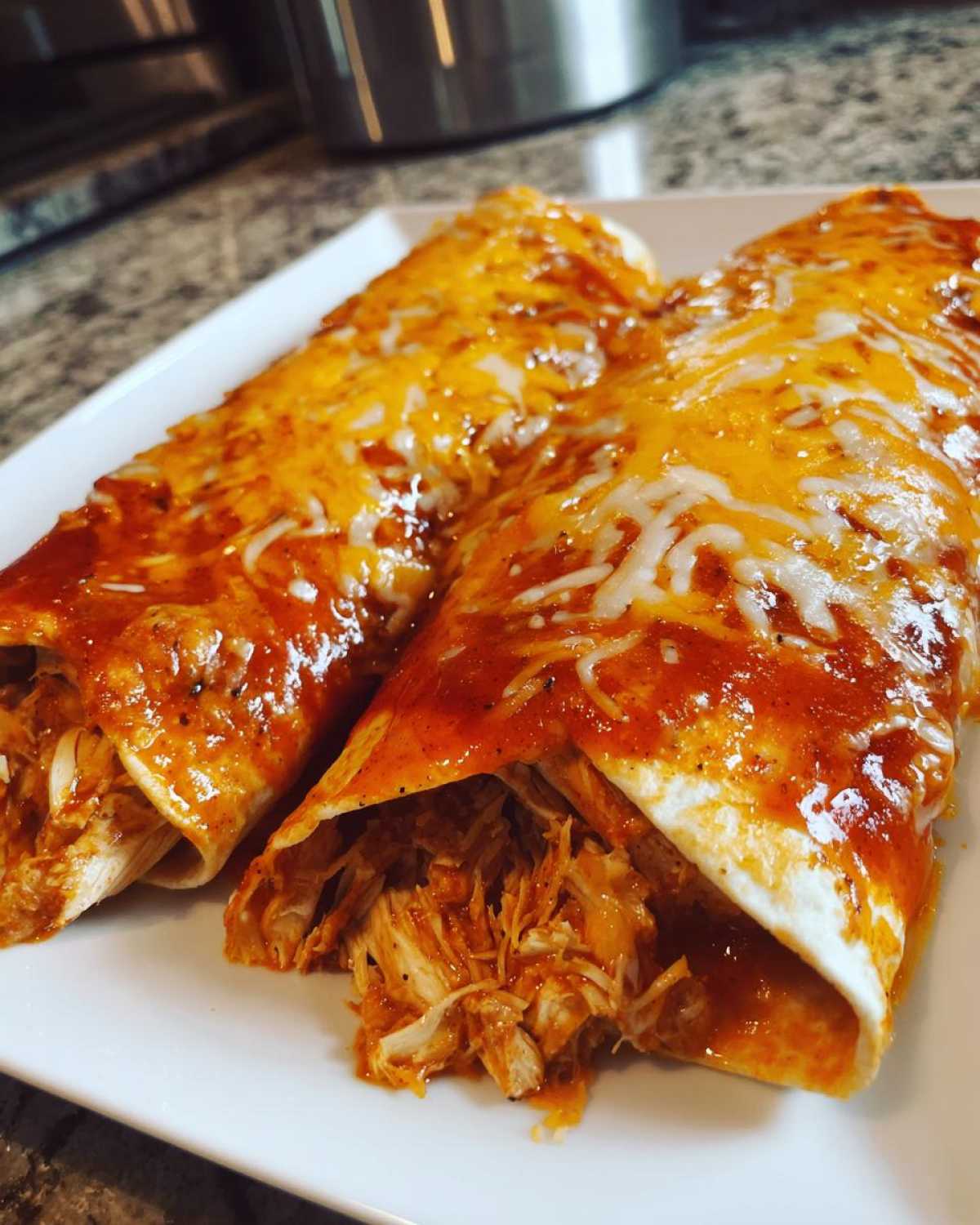 Two rolled easy chicken enchiladas covered in red sauce and melted cheddar cheese on a white plate.