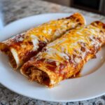 Two saucy easy chicken enchiladas covered in melted cheddar and Monterey Jack cheese served on a white plate.