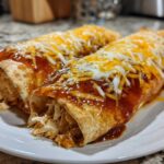 Two rolled easy chicken enchiladas covered in red sauce and shredded melted cheddar and Monterey Jack cheese.