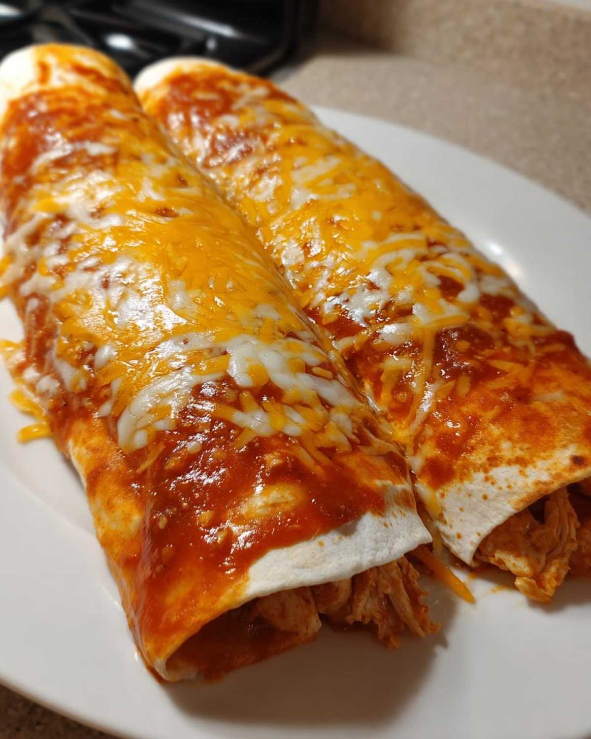 Close-up of two rolled easy chicken enchiladas covered in red sauce and melted cheddar and Monterey Jack cheese.